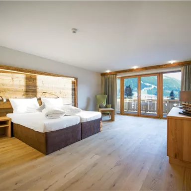 Ein modernes Hotelzimmer mit zwei Betten und Holzaccents. Große Fenster bieten einen Blick auf die umliegende Landschaft.