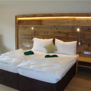 Ein gemütliches Schlafzimmer mit zwei Betten und einer Holzverkleidung an der Wand. Die sanfte Beleuchtung sorgt für eine angenehme Atmosphäre.