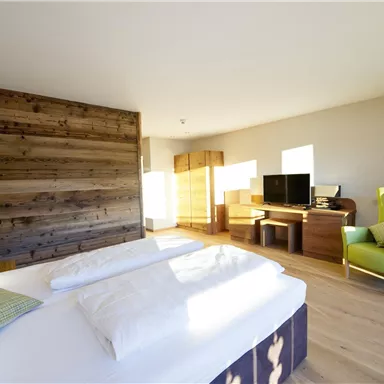 Ein modernes Schlafzimmer mit einem großen Bett und einem Holzpaneel. Der Raum ist hell und minimalistisch eingerichtet, mit einem gemütlichen Sessel und einem Schreibtisch.