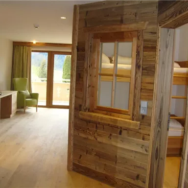 Ein modern eingerichteter Raum mit Holzverkleidung und großen Fenstern. Im Hintergrund ist ein gemütlicher Sessel und ein Etagenbett zu sehen.