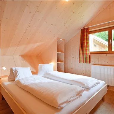 Ein gemütliches Schlafzimmer mit einem Doppelbett und hellen Holzvertäfen. Große Fenster lassen viel Tageslicht herein.