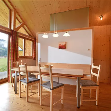 Ein helles, modernes Esszimmer mit Holzverkleidung. Große Fenster bieten einen Blick auf die umliegende Landschaft.
