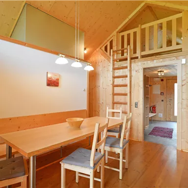 Ein gemütlicher Raum mit einer Holzdecke und einem Esstisch. Eine Treppe führt zu einem oberen Bereich.