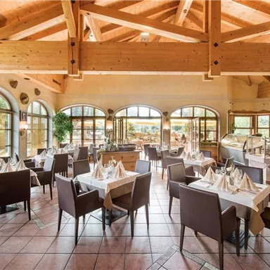 Eine elegante Restaurant-Umgebung mit Holzbalken und großen Fenstern. Tische sind schön gedeckt und laden zum Essen ein.