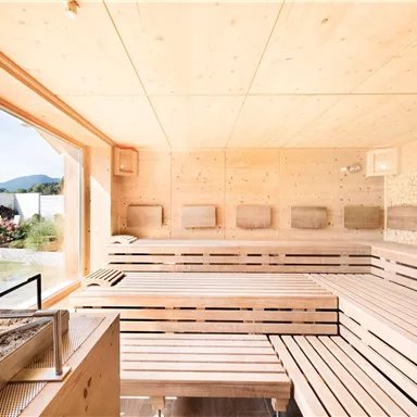 Eine moderne Sauna mit Holzverkleidung und großen Fenstern. Im Hintergrund ist eine ruhige Landschaft zu sehen.