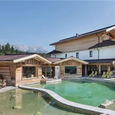 Eine moderne Chalet-Architektur mit einem schönen, natürlichen Pool und einer großzügigen Gartenlandschaft. Im Hintergrund sind majestätische Berge zu sehen.