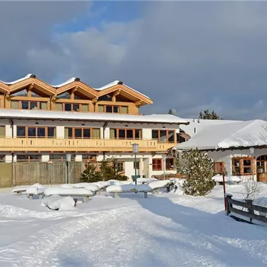 Ein gemütliches Hotel im Schnee mit viel Holz und großen Fenstern. Die Umgebung ist winterschön und die Landschaft ist von Schnee bedeckt.