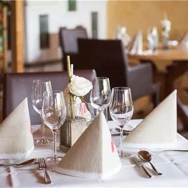 Ein elegant gedeckter Tisch im Restaurant mit weißen Tischdecken und dekorativen Servietten. Gläser und Besteck sind sorgfältig angeordnet, was eine einladende Atmosphäre schafft.