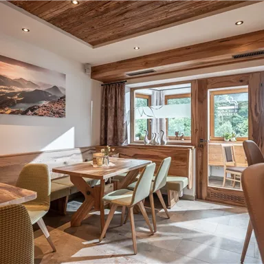 Ein gemütliches Café mit Holzmöbeln und Blick auf die Natur. Große Fenster sorgen für viel Tageslicht und eine einladende Atmosphäre.