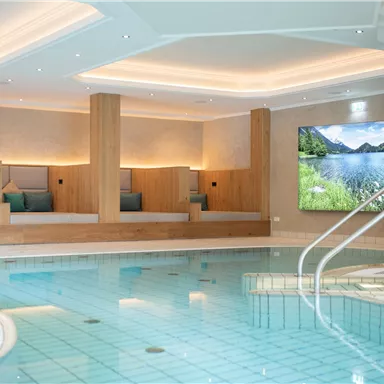 A modern wellness area with a swimming pool and comfortable lounging areas. On the wall, there is a large screen displaying a landscape photograph.