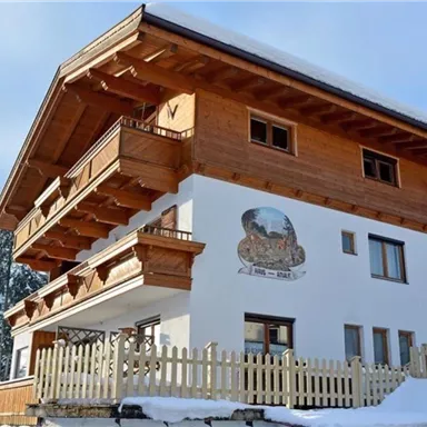 Ein gemütliches Chalet im alpinen Stil mit Holzbalkonen. Umgeben von schneebedeckten Bäumen und einer klaren Winteratmosphäre.