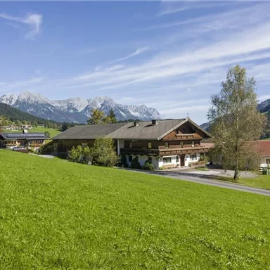 An idyllic house in a green meadow with a view of the mountains. The landscape is calm and picturesque with a blue sky.