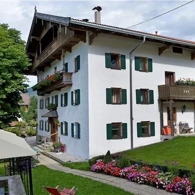 A charming three-story building with white walls and green shutters. The garden is adorned with colorful flowers and a playground.