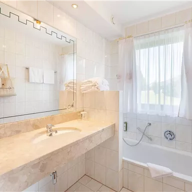 A modern bathroom with a bathtub and a large mirror. White towels and bright curtains create an inviting atmosphere.