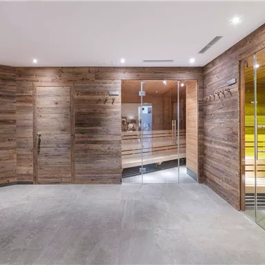 A modern sauna area with wooden paneling and soft lighting. The glass walls provide a view of the sauna and the inviting room.