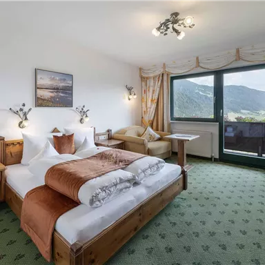 A cozy hotel room with two beds, a table, and a chair. The window offers a view of the mountains.