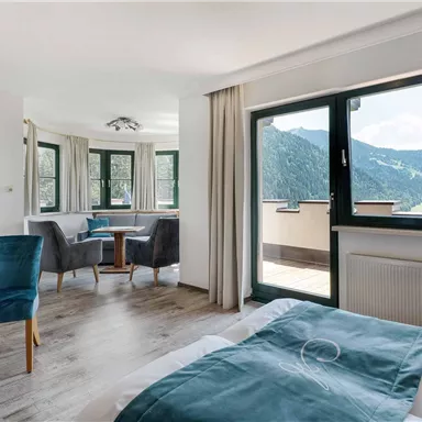 A modern room with a sleeping area and a living room. Large windows provide a view of the mountains and ensure plenty of daylight.