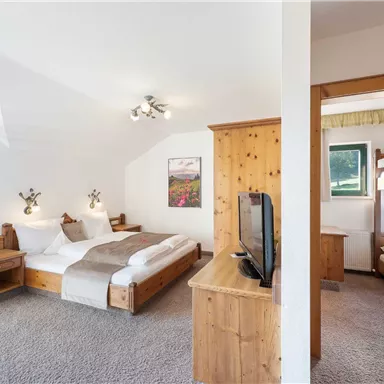 A modern room with two beds, a television, and a cozy wooden wardrobe. There is an adjacent room with a bunk bed, ideal for families.