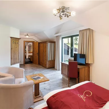 A spacious hotel room with a double bed, a television, and a cozy seating area. Large windows provide plenty of daylight and offer a view outside.