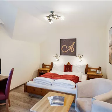 A cozy hotel room with a double bed and red bedding. There is a desk, a television, and a comfortable armchair.