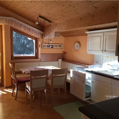 Eine helle und einladende Küche mit Holzdecke und großen Fenstern. Der Essbereich ist mit einem Tisch und Stühlen ausgestattet.