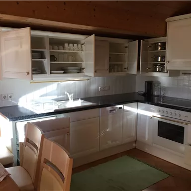 Eine helle Küche mit weißen Schränken und modernen Geräten. Ein Esstisch mit Stühlen befindet sich im Vordergrund.