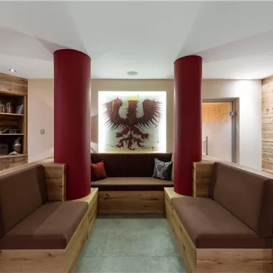 A modern reception area with cozy wooden seating and comfortable cushions. In the background, there is a stylized coat of arms featuring an eagle.