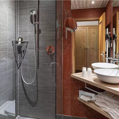 A modern bathroom with a glass shower and two sinks. The walls are designed in soothing shades of gray.