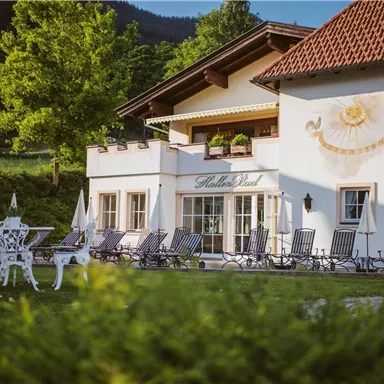 A charming house with a bright outdoor area and elegant loungers. The green surroundings and the mountains in the background create a relaxing atmosphere.