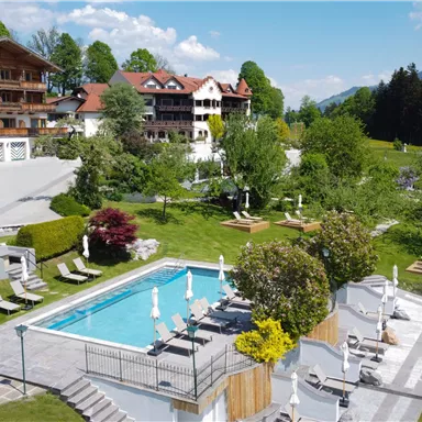 A beautiful outdoor area with a swimming pool and loungers. In the background, well-kept gardens and the mountains are visible.