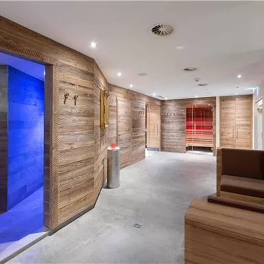 A modern wellness area with wooden paneling and a relaxing atmosphere. In the background, sauna and shower areas are visible.