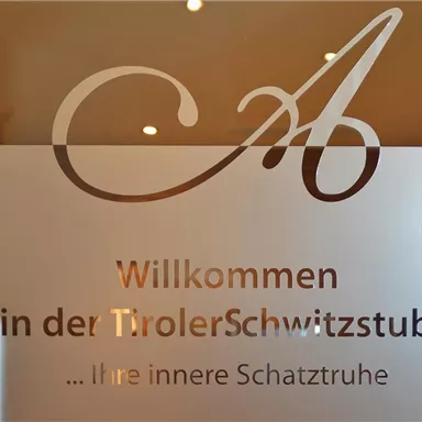 Influential sign on a glass door. It welcomes guests to the "Tyrolean Sweat Room" and points to a relaxing atmosphere.