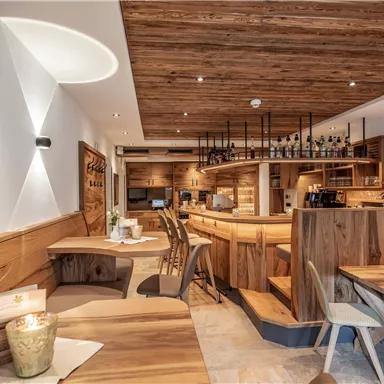 Ein gemütliches Restaurant mit Holzmöbeln und warmem Licht. Der Bartresen ist gut sichtbar und die Atmosphäre ist einladend.
