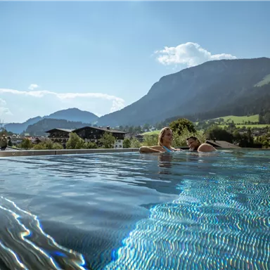 A beautiful infinity pool with a view of the mountains. The sun is shining and the landscape is green and inviting.