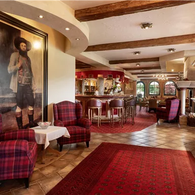 A cozy interior with red armchairs and a large painting on the wall. In the background, there is a bar with wooden shelves and an inviting atmosphere.