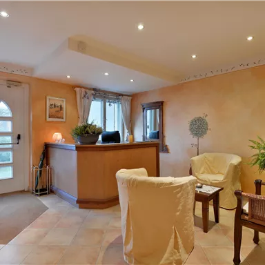 Ein einladender Empfangsbereich mit einem Empfangstresen und bequemen Sitzgelegenheiten. Die warmen Farben der Wände schaffen eine gemütliche Atmosphäre.