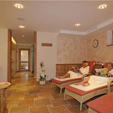 Ein ruhiger Wellnessbereich mit bequemen Liegen. Zwei Personen entspannen in Bademänteln und lesen Zeitschriften.