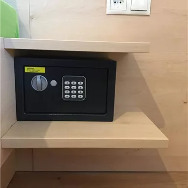 A safe with a combination lock is standing on a shelf. Above it, there is a power outlet on the wall.