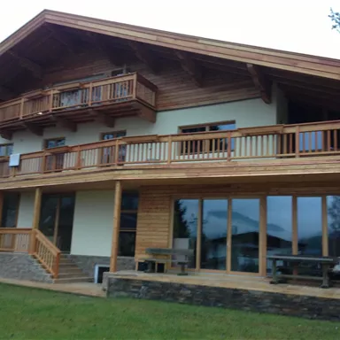 Ein modernes Holzhaus mit großzügigem Balkon und großen Fenstern. Die Terrasse ist umgeben von grünem Rasen.