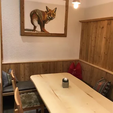 A cozy dining area with a large wooden table and benches. A painting of a fox hangs on the wall.