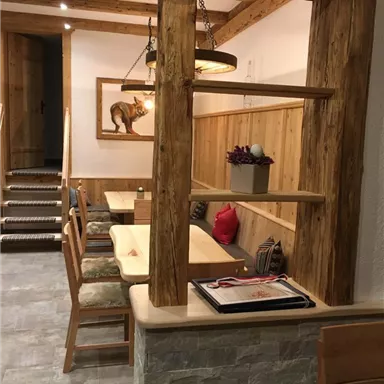 A cozy dining area with wooden shelves and comfortable chairs. The room features warm colors and an inviting atmosphere.