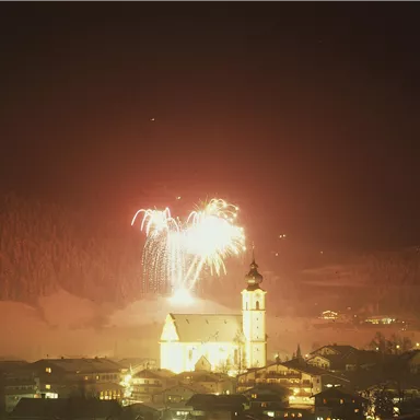 Ein Feuerwerk über einer malerischen Stadt im Winter. Die Kirche strahlt im Licht der bunten Feuerwerkskörper.