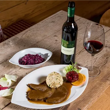 Ein köstliches Gericht mit zartem Fleisch, Beilagen und einer Portion Preiselbeeren. Daneben steht eine Flasche Rotwein und ein Glas.