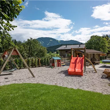 Ein schöner Spielplatz in einer grünen Umgebung. Es gibt Schaukeln, Rutschen und einen herrlichen Ausblick auf die Berge.