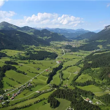 A picturesque valley with green meadows and gentle hills. In the background, impressive mountains and a blue sky can be seen.