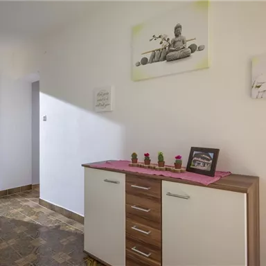 A bright hallway with a white cabinet and a wooden surface. Small plants and picture frames are on a pink tablecloth.