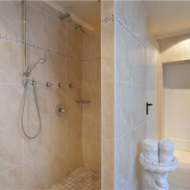 Moderne Dusche in einem eleganten Badezimmer. Die Wände sind mit beige Fliesen verkleidet und es gibt eine Pflanze in der Ecke.