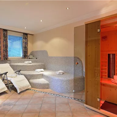 Ein entspannender Wellnessbereich mit Liegen und einem Sauna-Bereich. Die warmen Farben und die gemütliche Atmosphäre laden zum Relaxen ein.