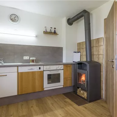 A modern kitchen with a wooden floor and a kitchenette. An oven is in the corner and emits warmth.