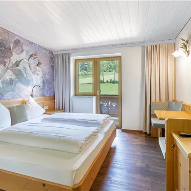 A bedroom with two single beds, wooden furniture, and a window that overlooks a green landscape. The walls are decorated with colorful wallpaper that adds a modern touch.